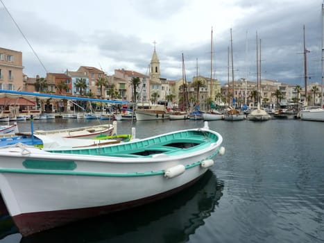 Colorful boats, port, buildings and famous bell tower of the church at Sanary-sur-mer, south of France, by cloudy weather