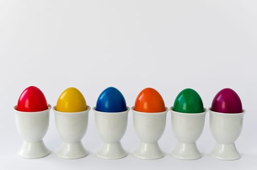 Six colorful eggs in white egg cups (cutout)