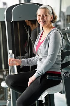 Senior woman relax at gym sitting by fitness machine