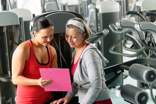 Senior woman with personal trainer looking exercise chart at gym