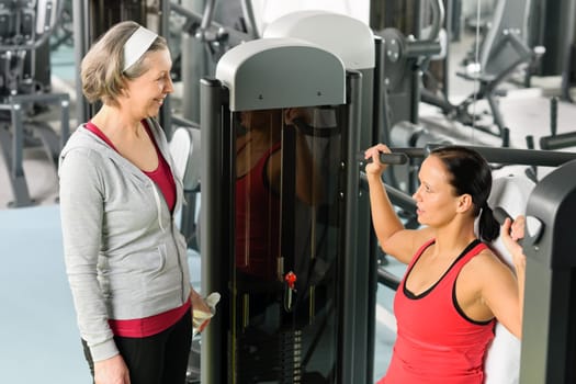 Personal trainer at fitness center showing exercise to senior woman