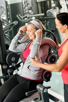 Senior woman at gym exercise with personal trainer on machine