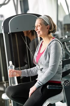Senior woman relax at gym sitting by fitness machine