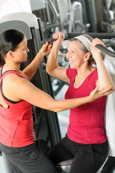 Personal trainer assist senior woman exercising on machine at gym