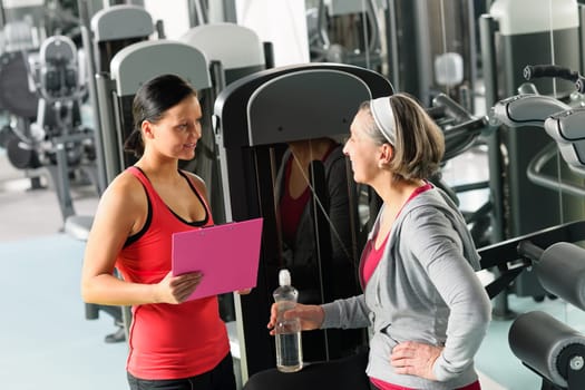 Senior woman with trainer discuss personal plan at gym