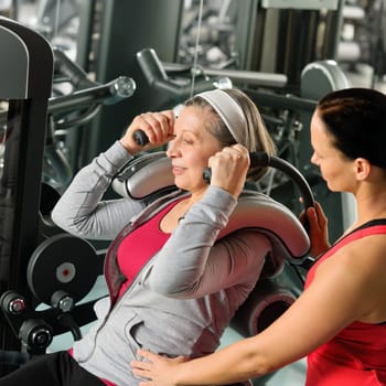 Senior woman at gym exercise with personal trainer on machine