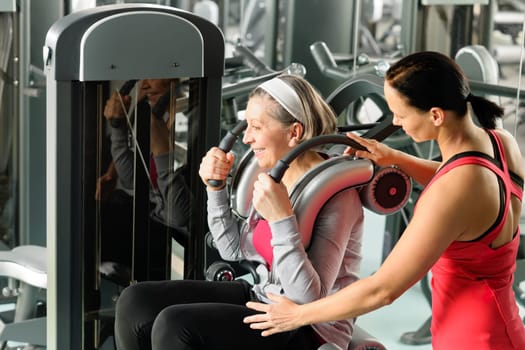Senior woman at gym exercise with personal trainer on machine