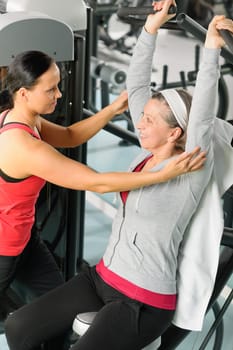 Senior woman at fitness center exercise on machine with trainer