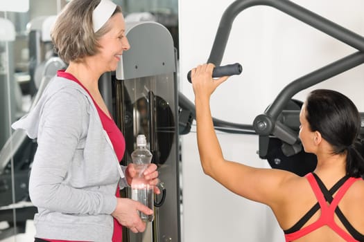 Personal trainer at fitness center showing exercise to senior woman