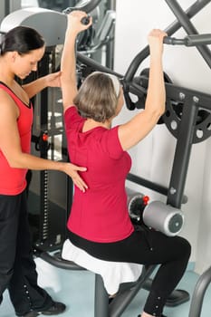 Fitness center personal trainer senior woman exercise shoulder on machine