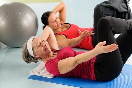 Fitness center senior woman exercise sit ups with personal trainer