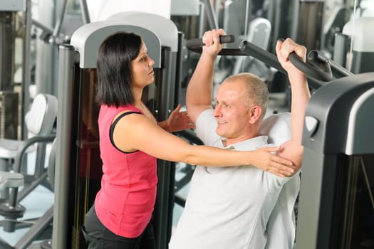 Fitness center personal trainer assist man exercise shoulder on machine