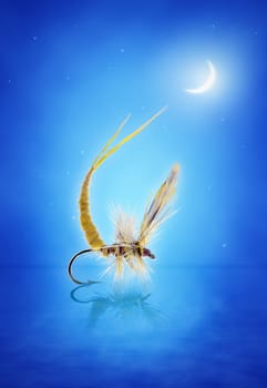 Yellow small handtied may fly nymph over the water. Dark sky with stars and moon at the background