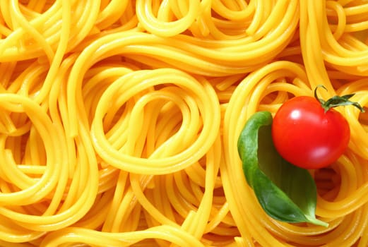 Closeup of freshly boiled spaghetti coiled in random patterns for an interesting background. With basil and tomato