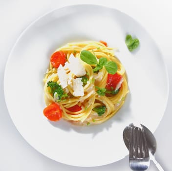 Overhead view of a prepared plate of spaghetti broccoli with parmesan ready for serving garnished with tomatoes and basil