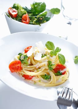 A plate of spaghetti broccoli ready for serving garnished with tomatoes, parmesan cheese and basil