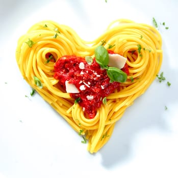 Spaghetti with tomato and cheese sauce garnished with basil arranged in coils into a heart shape for love