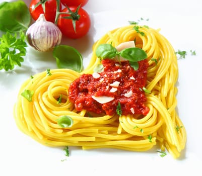 Cooked spaghetti arranged in a heart shape topped with tomato sauce and fresh basil
