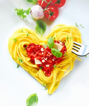 Cooked spaghetti carefully arranged in a heart shape and topped with tomato sauce accompanied by raw ingredients to the side