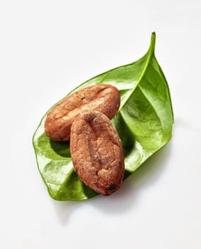Two cacao beans on a green cocoa leaf isolated on white background