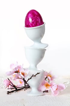 Three plain white china eggcups balanced precriously one on top of the other with a pink marbled Easter Egg and pink blossom.