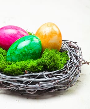 Three colourful marbled Easter eggs on green moss in a nest constructed of interwoven twigs
