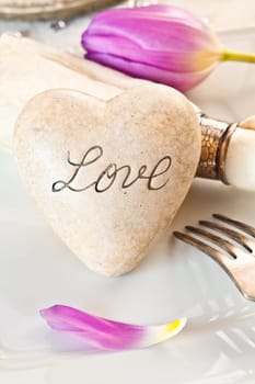 Love table setting with spring flower and stone heart inscribed with the word Love conceptual of valentines or a wedding card