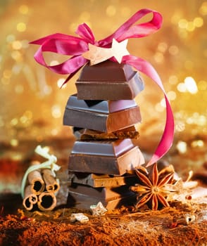 Festive chocolate tower topped with a pink bow and decorated with dried spices and cinnamon against a bokeh of festive lights.