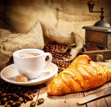 Coffee cup with a croissant and fresh coffee beanson a brown background