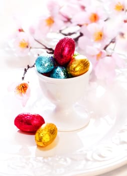 An eggcup full of tiny colourful foil wrapped chocolate Easter Eggs with cherry blossom
