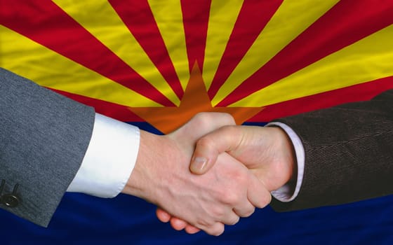 two businessmen shaking hands after good business investment  agreement in america, in front US state flag of arizona