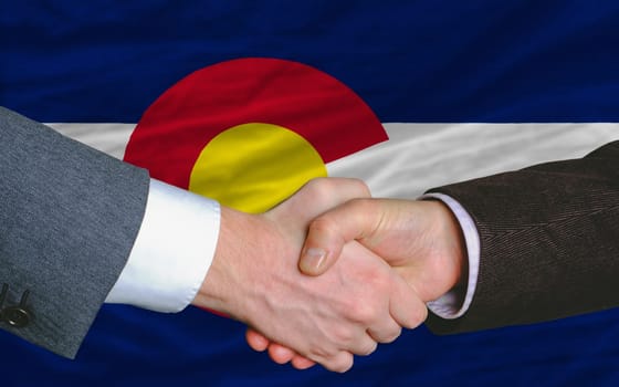 two businessmen shaking hands after good business investment  agreement in america, in front US state flag of colorado