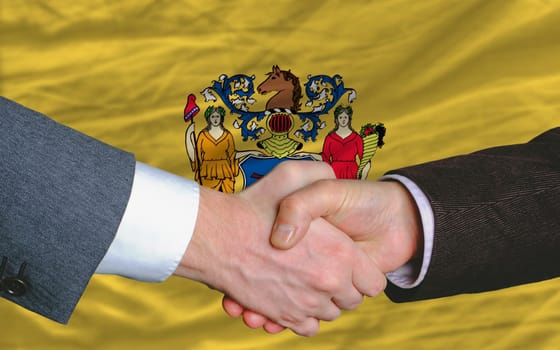 two businessmen shaking hands after good business investment agreement in front US state flag of new jersey