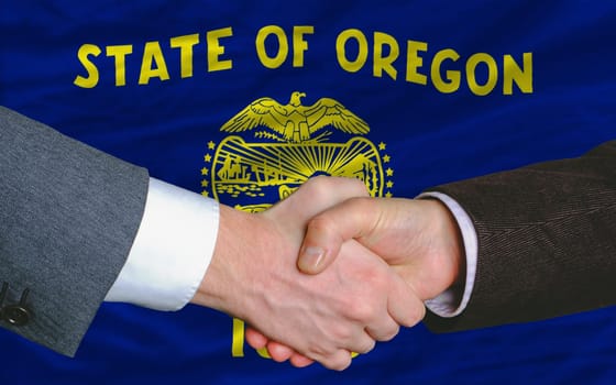two businessmen shaking hands after good business investment agreement in front US state flag of oregon