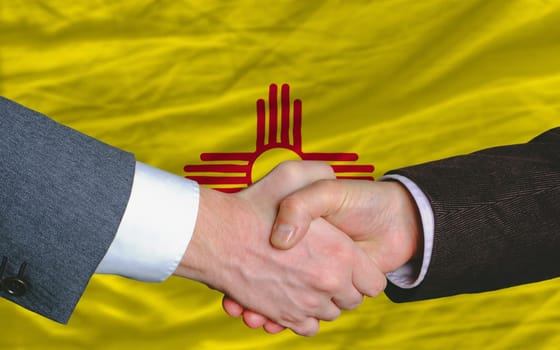 two businessmen shaking hands after good business investment agreement in front US state flag of new mexico