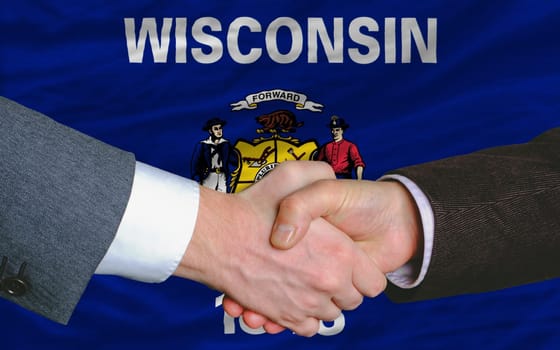 in front of american state flag of wisconsin two businessmen handshake after good deal