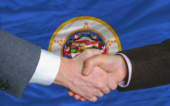 two businessmen shaking hands after good business investment  agreement in front US state flag of minnesota