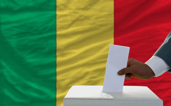 man putting ballot in a box during elections  in front of national flag of malawi