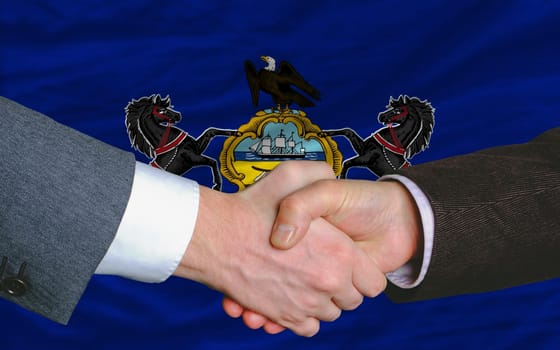 two businessmen shaking hands after good business investment agreement in front US state flag of pennsylvania