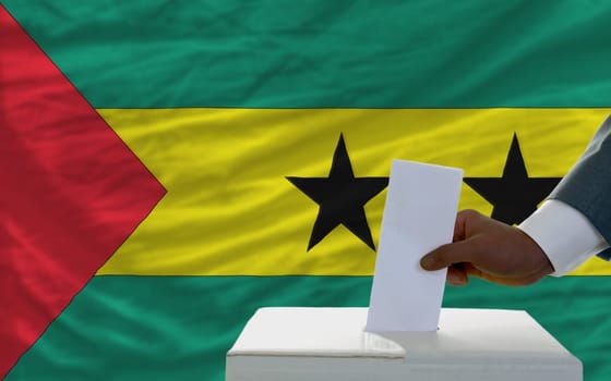 man putting ballot in a box during elections  in front of national flag of sao tome principe