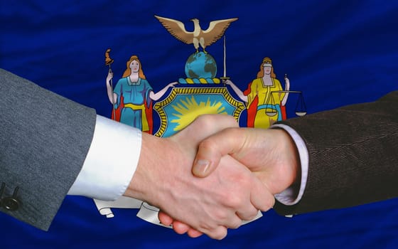 two businessmen shaking hands after good business investment agreement in front US state flag of new york