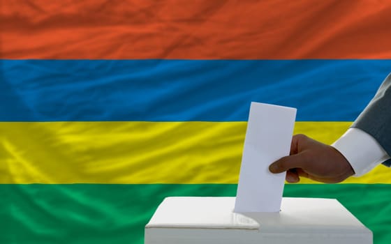 man putting ballot in a box during elections  in front of national flag of mauritius