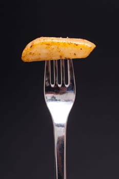 Spiced potato with fork against a black background