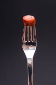 Sausage pepper biter and a fork against black background