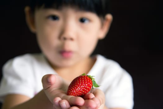 Happy little girl put a strawberry in her hand. The focus is on the strawberry.