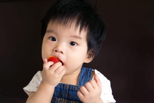 Photo of a little baby girl eating strawberry