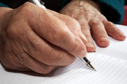 Old hands writing with an ink pen in a notebook