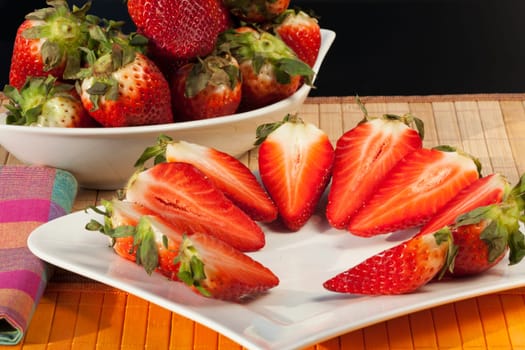 Whole and half strawberries in a bowl and on a plate