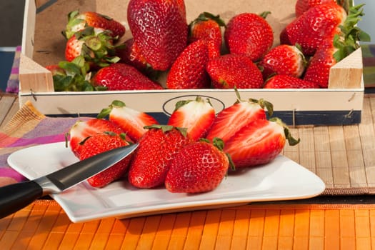Whole and half strawberries in a wooden box and on a plate with a knife