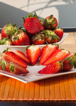 Whole and half strawberries in a bowl and on a plate